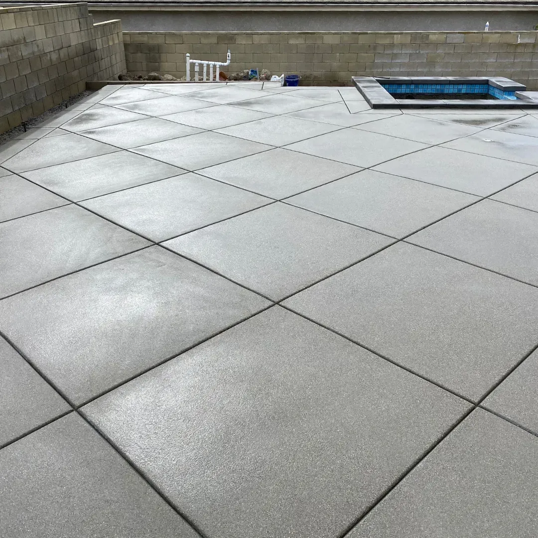 Concrete patio with diamond pattern, near a small pool and a block wall.
