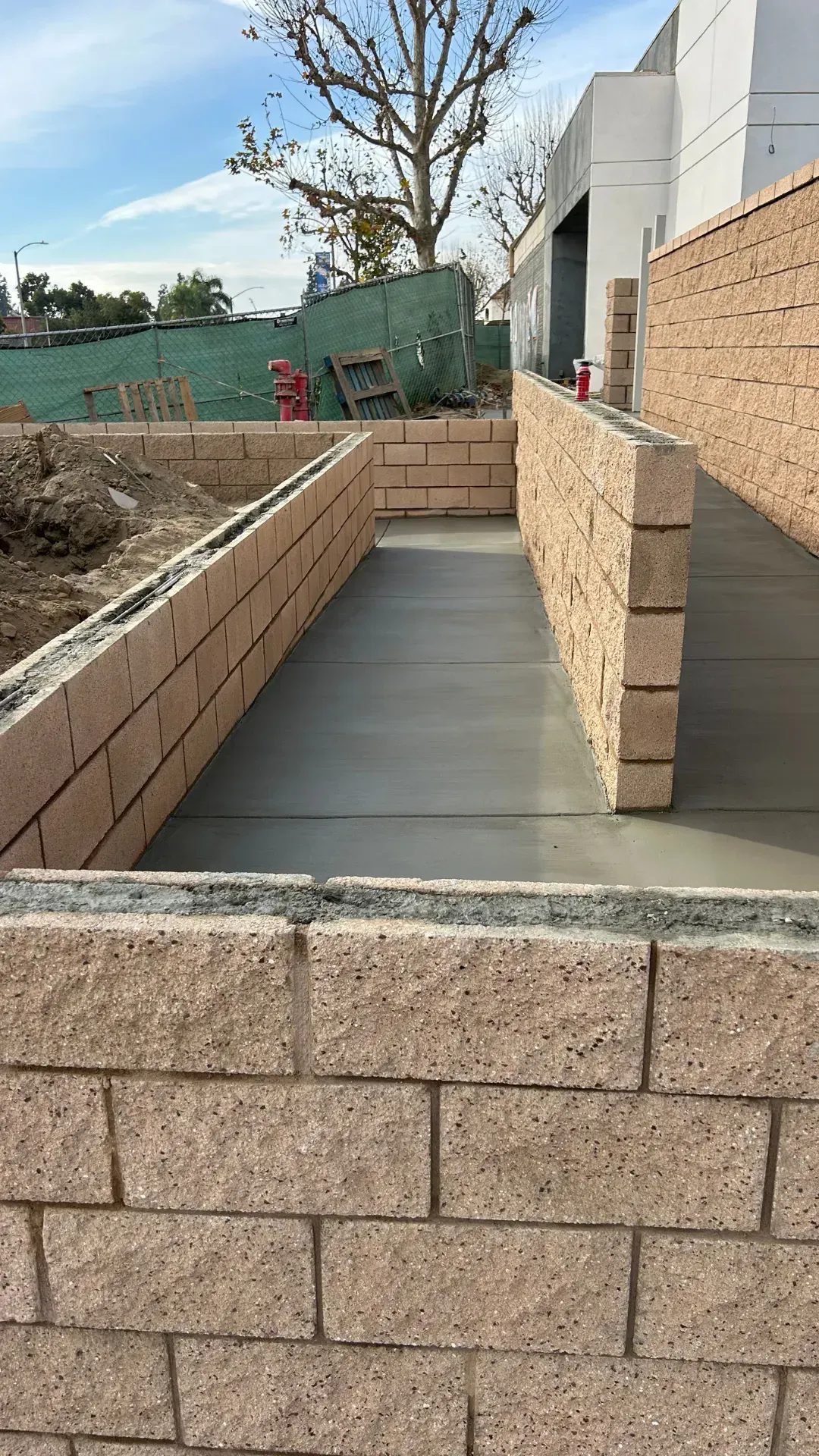 Concrete ramp construction with brick walls. Gray concrete path between tan brick retaining walls.