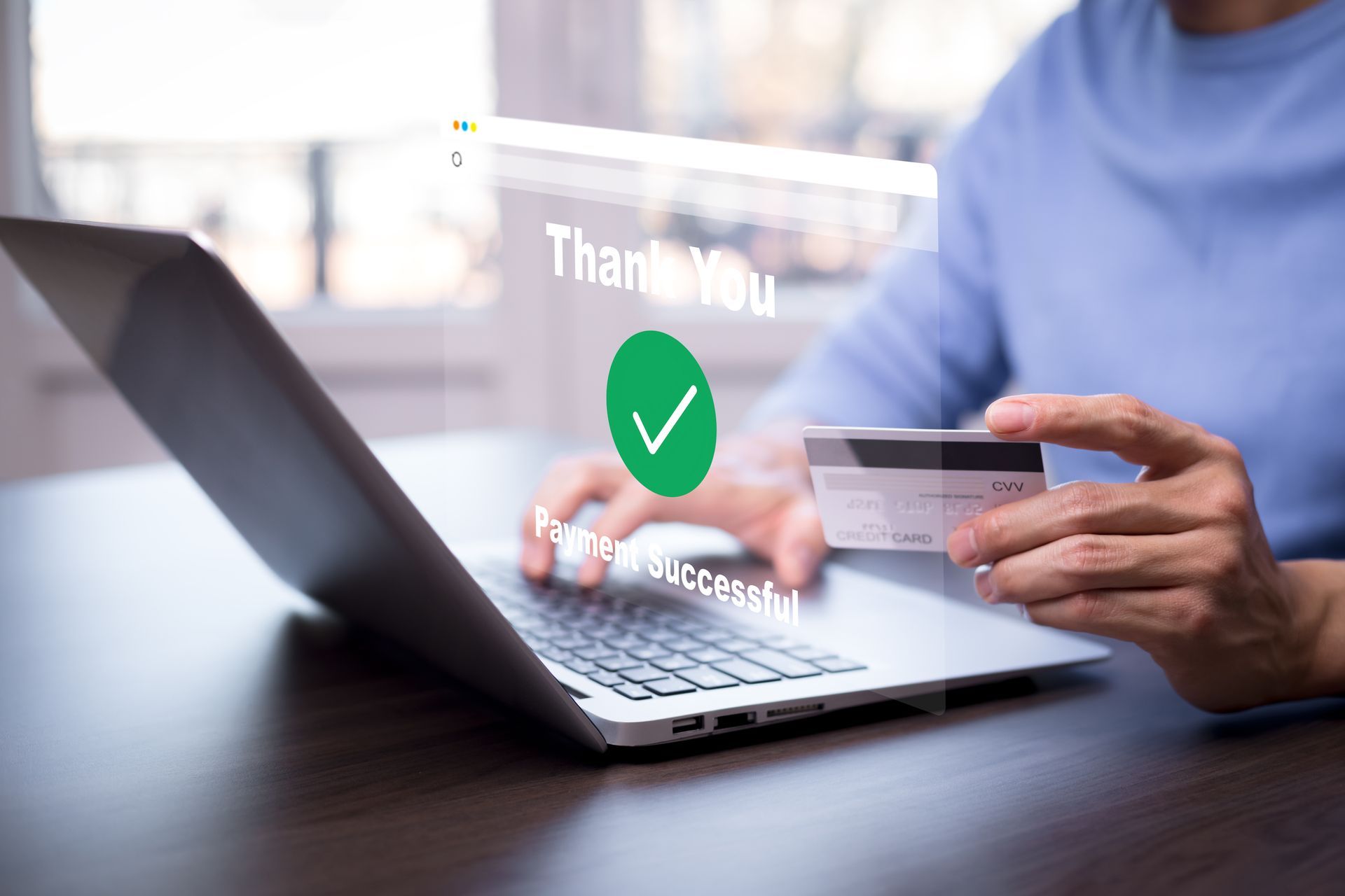 A person is holding a credit card in front of a laptop computer.