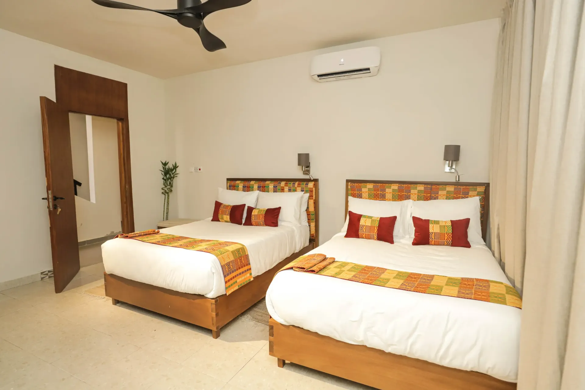 Two beds double in a room, white walls, wooden headboards, colorful bedding, and air conditioner,