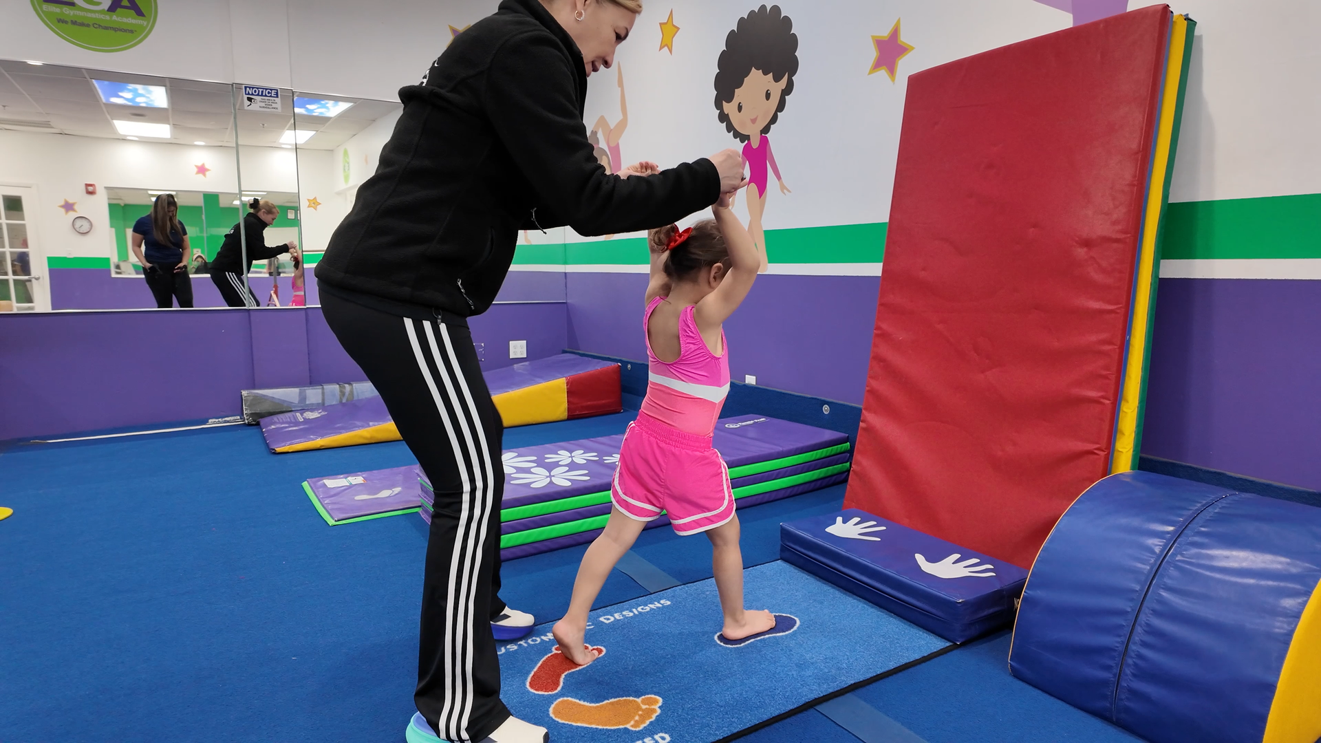 Una mujer está ayudando a una niña a mantener el equilibrio en una viga de equilibrio en un gimnasio.