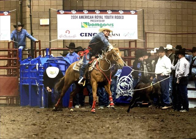 Rider on a bucking horse in a muddy rodeo arena, surrounded by handlers and blue barriers