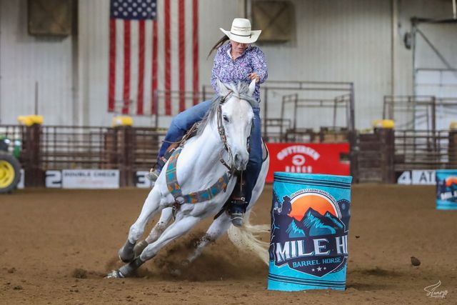 Cowgirl on a white horse racing around a barrel in an indoor rodeo arena