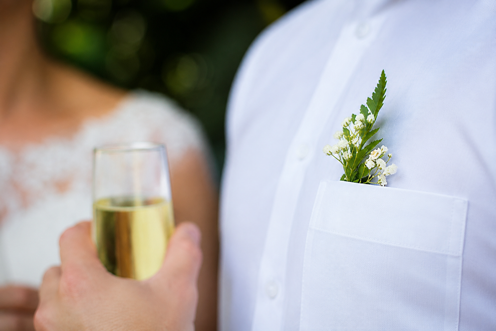 Camicia bianca con boutonnière verde, brinda con un calice di champagne durante un evento formale.