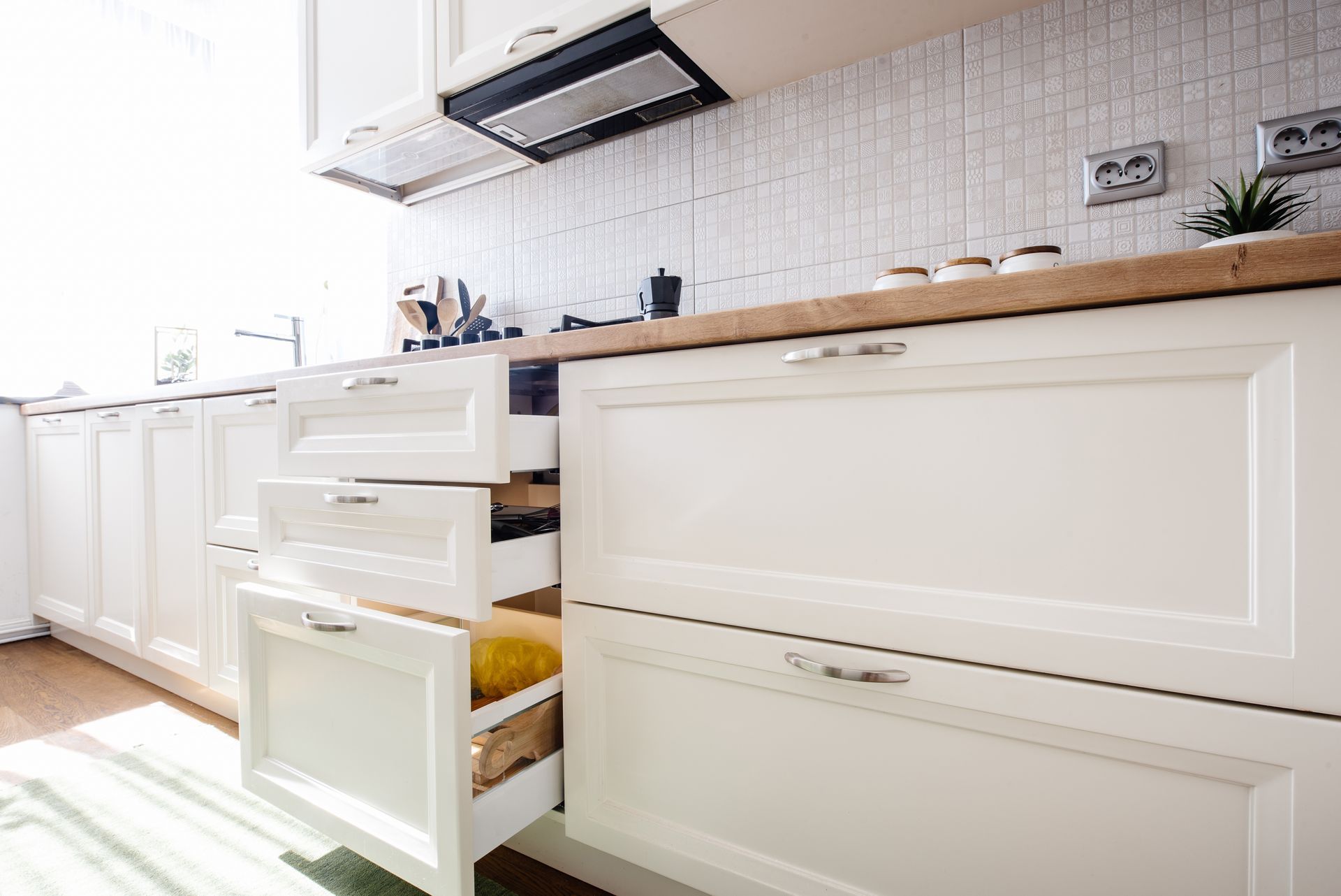 Bright white kitchen with open drawers, wood countertop, and tiled backsplash