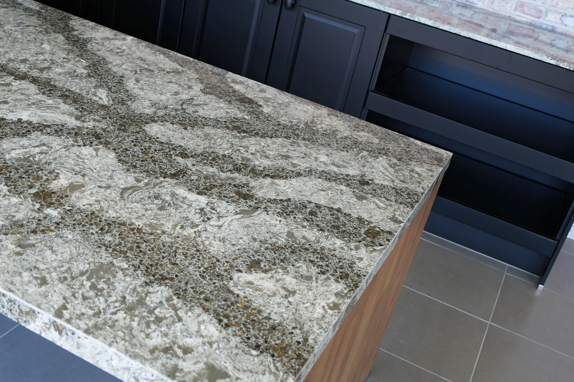 Granite kitchen countertop with gray veining beside dark cabinets and tile floor