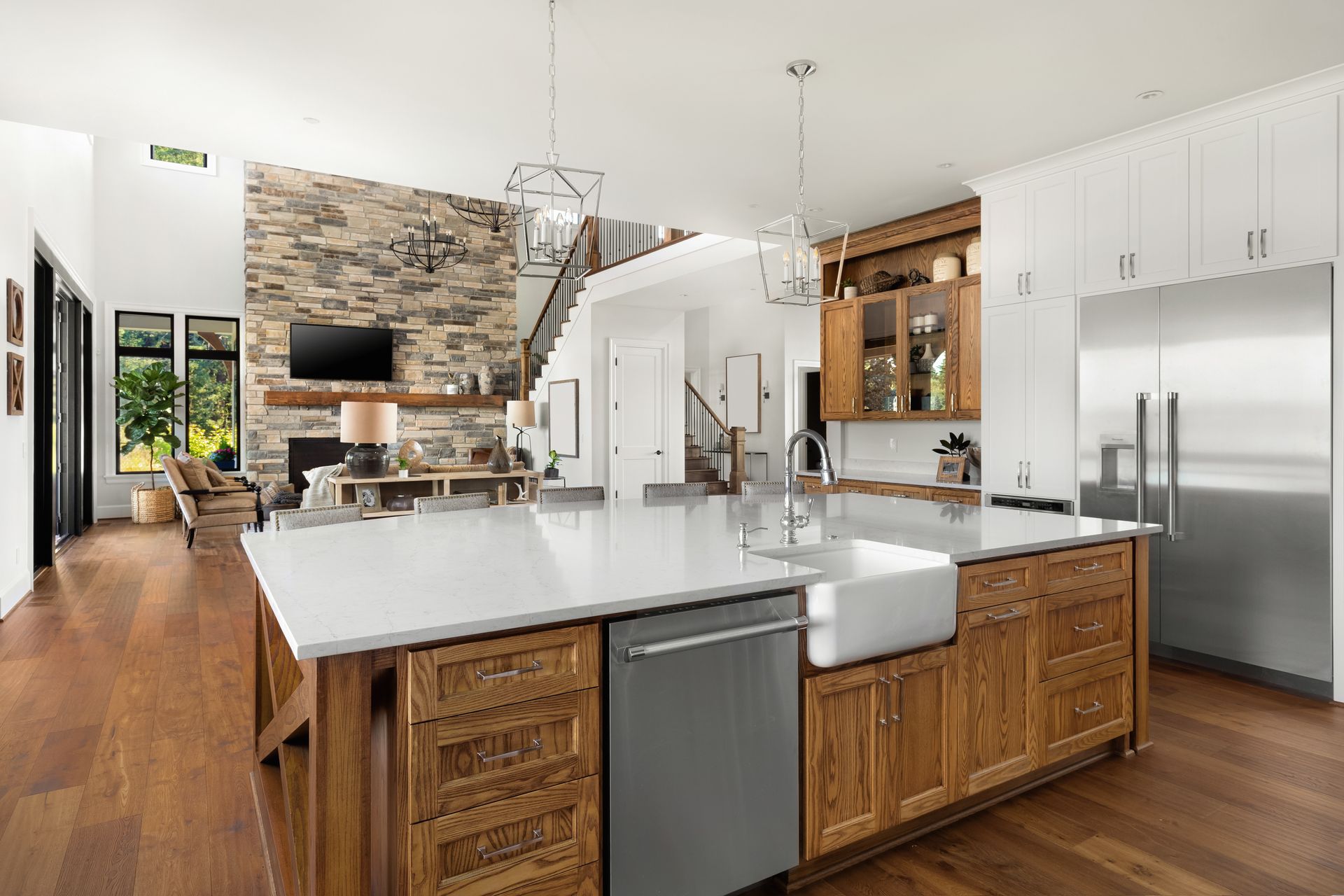Modern kitchen with white island, wood cabinets, stainless fridge, and stone fireplace in background