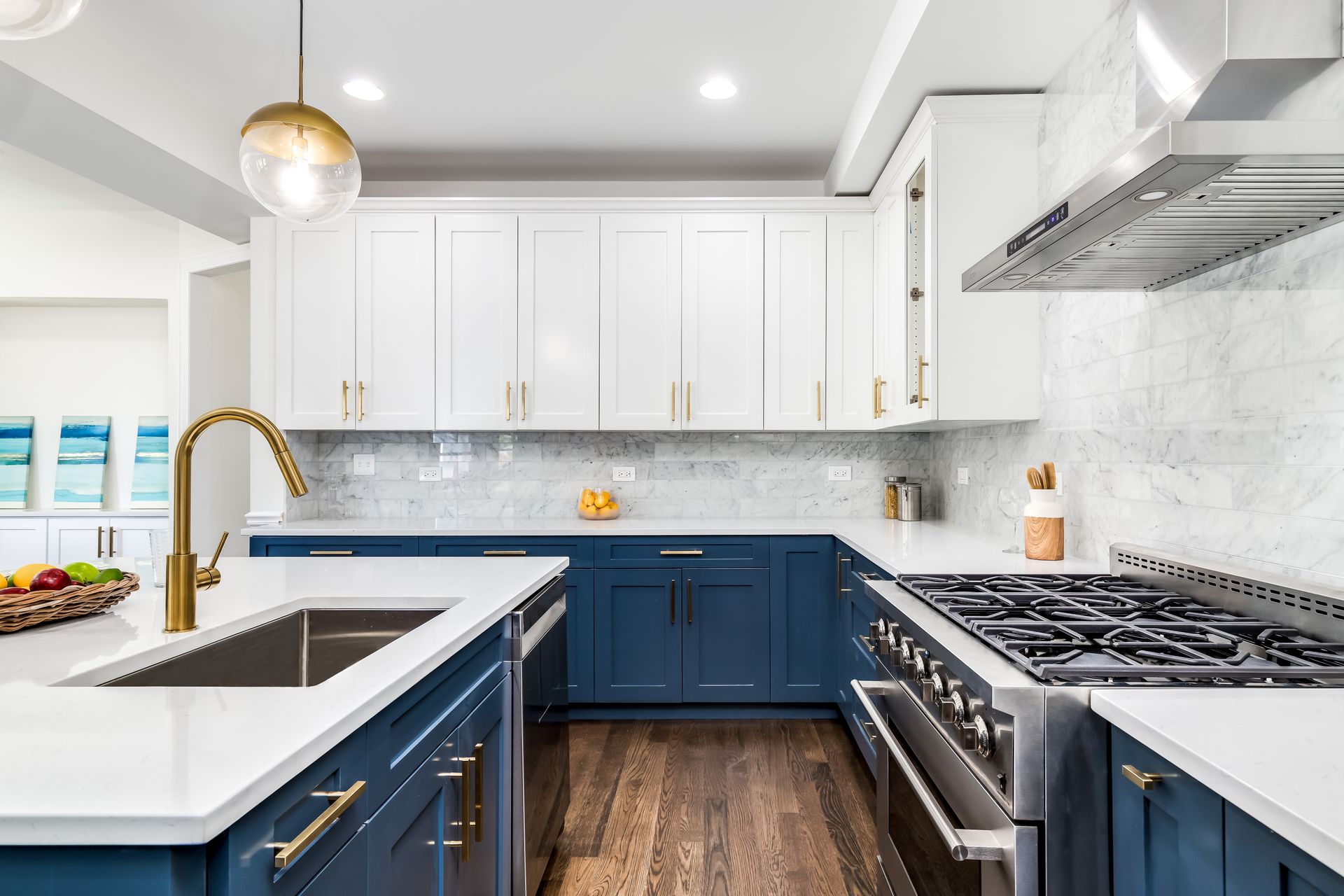 Bright modern kitchen with navy and white cabinets, marble island, gold faucet, and stainless steel stove.