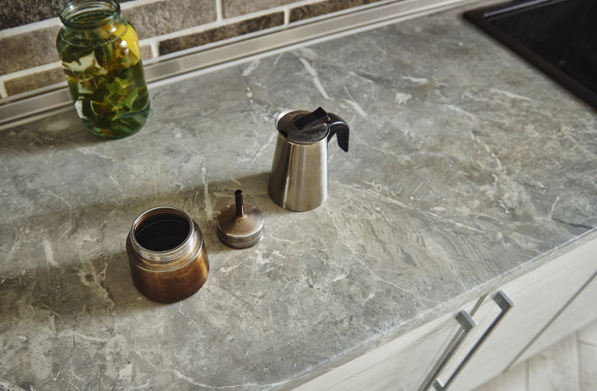 Marble kitchen counter with a moka pot, small jar, and glass jar of green pickles near the backsplash