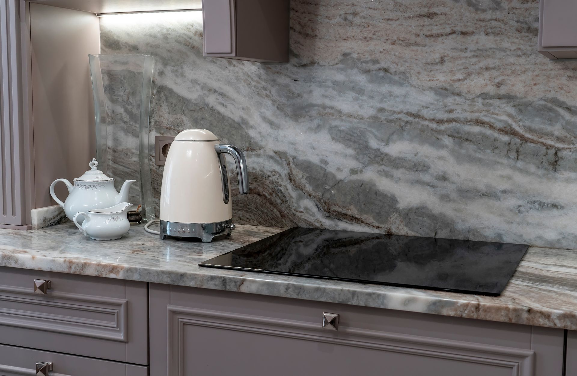 Kitchen countertop with white kettle and teapot beside a black sink and gray marble backsplash