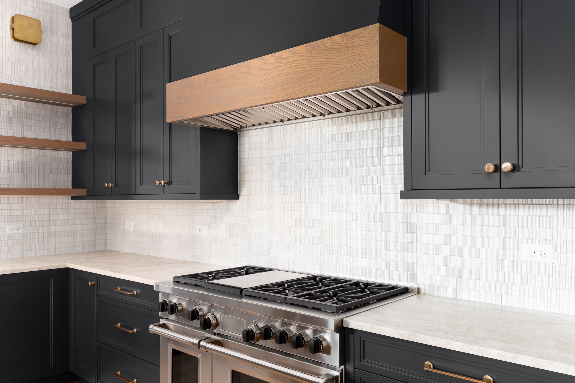 Modern kitchen with dark cabinets, white tile backsplash, wood range hood, and stainless steel stove.