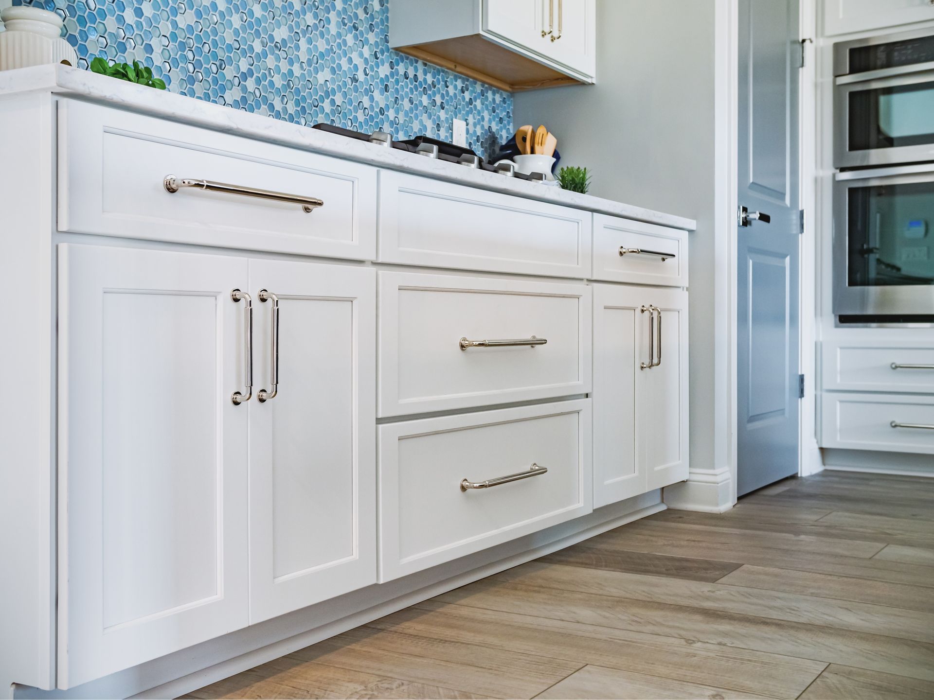 White kitchen cabinets with drawers, blue mosaic backsplash, and wood-look tile floor