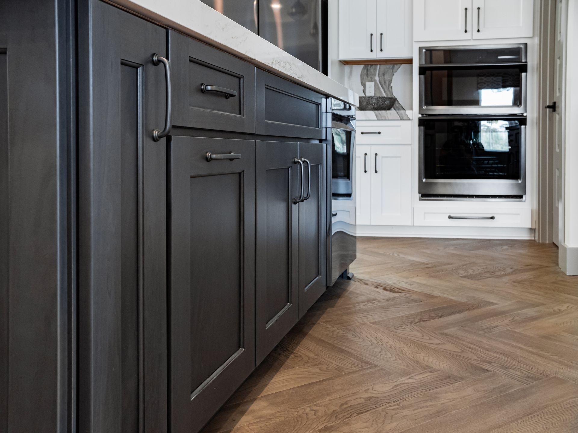 Modern kitchen with dark cabinets, white appliances, and herringbone wood flooring