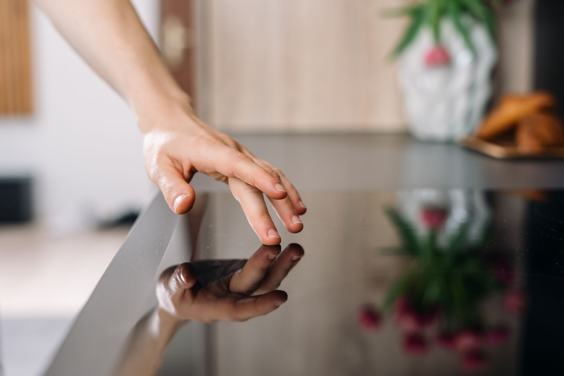 Hand reaching to touch a glossy black glass tabletop with a blurred home interior in the background