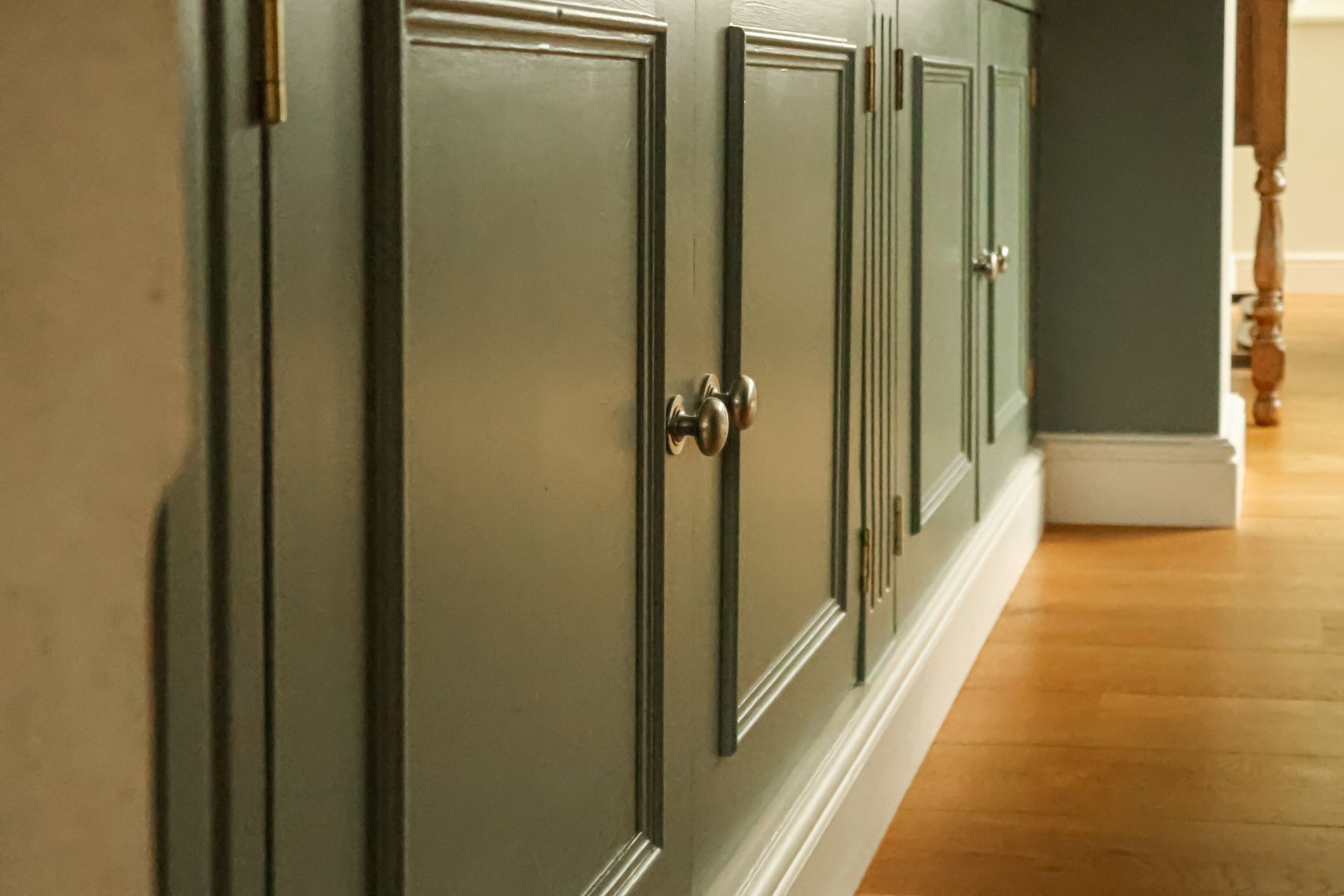 Gray paneled cabinet along a hallway with a wooden floor and white baseboard.