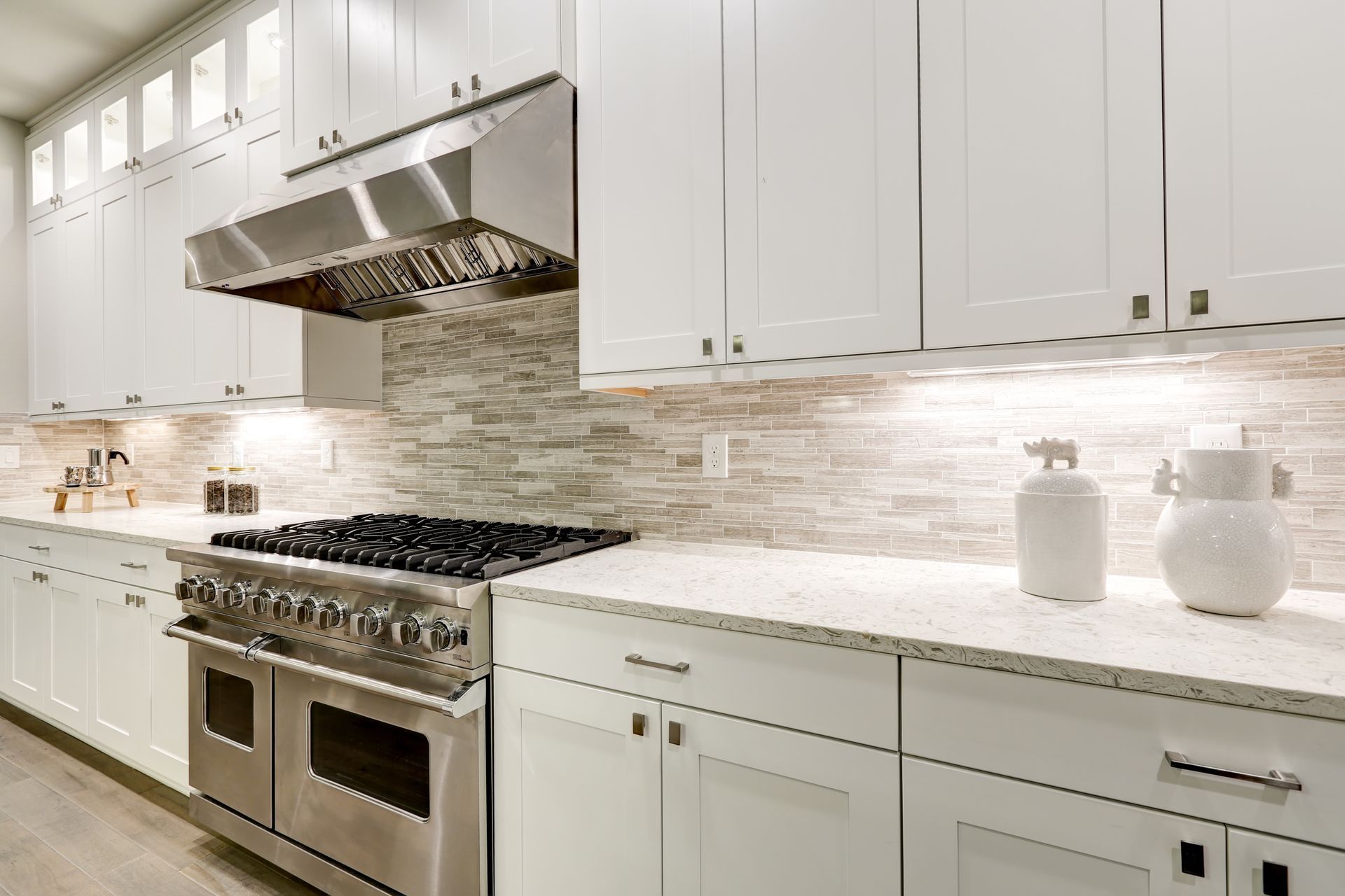 Bright white modern kitchen with stainless steel stove, range hood, and marble countertops