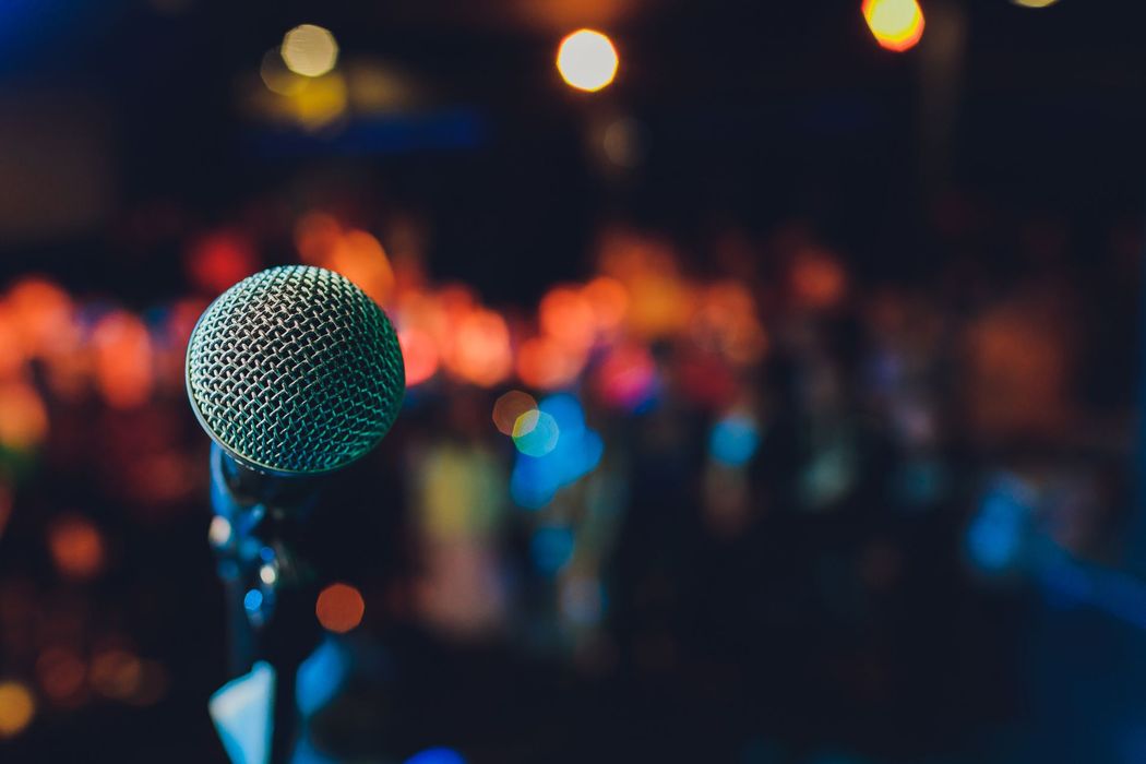 Microfono sul palco con luci colorate e sfocate del pubblico sullo sfondo.