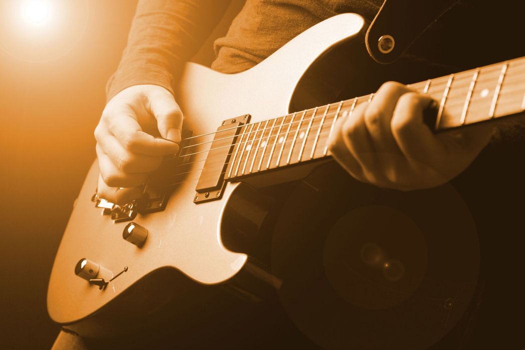 Primo piano di mani che suonano una chitarra elettrica bianca sotto le calde luci del palco.