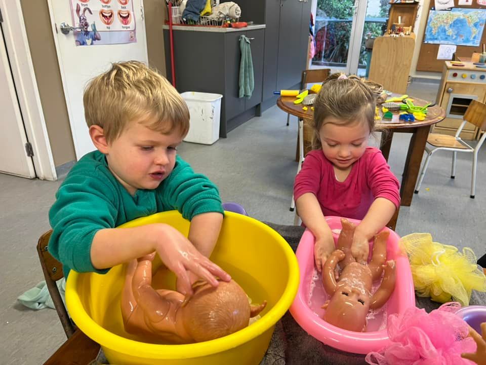 A boy and a girl are playing with dolls in a tub.