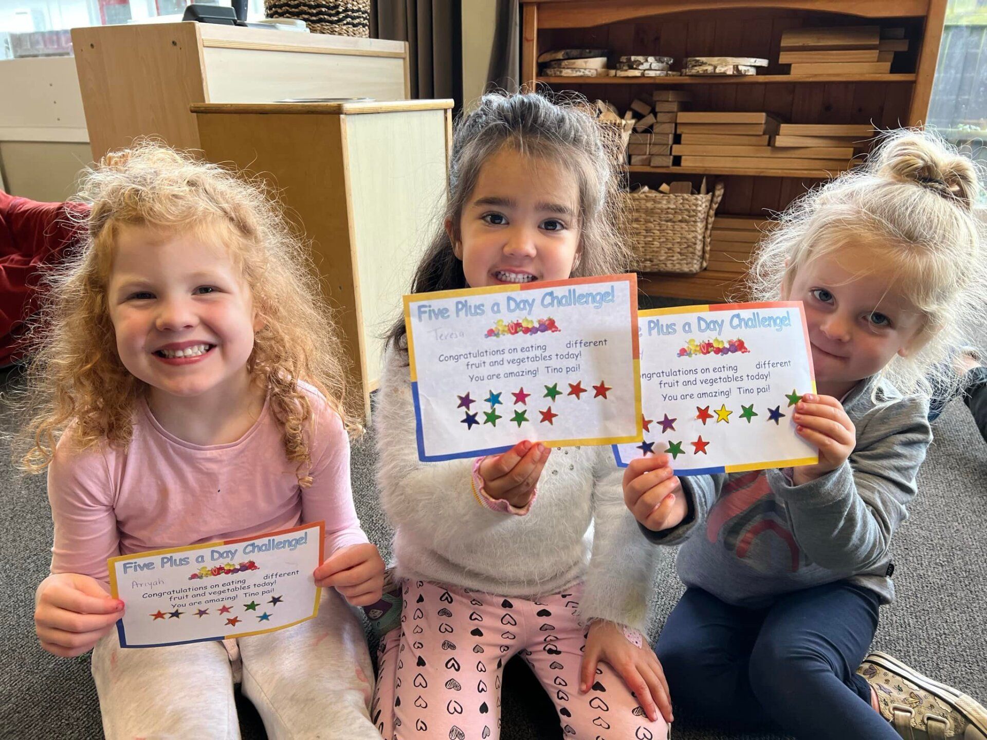 Three little girls are sitting on the floor holding up cards.