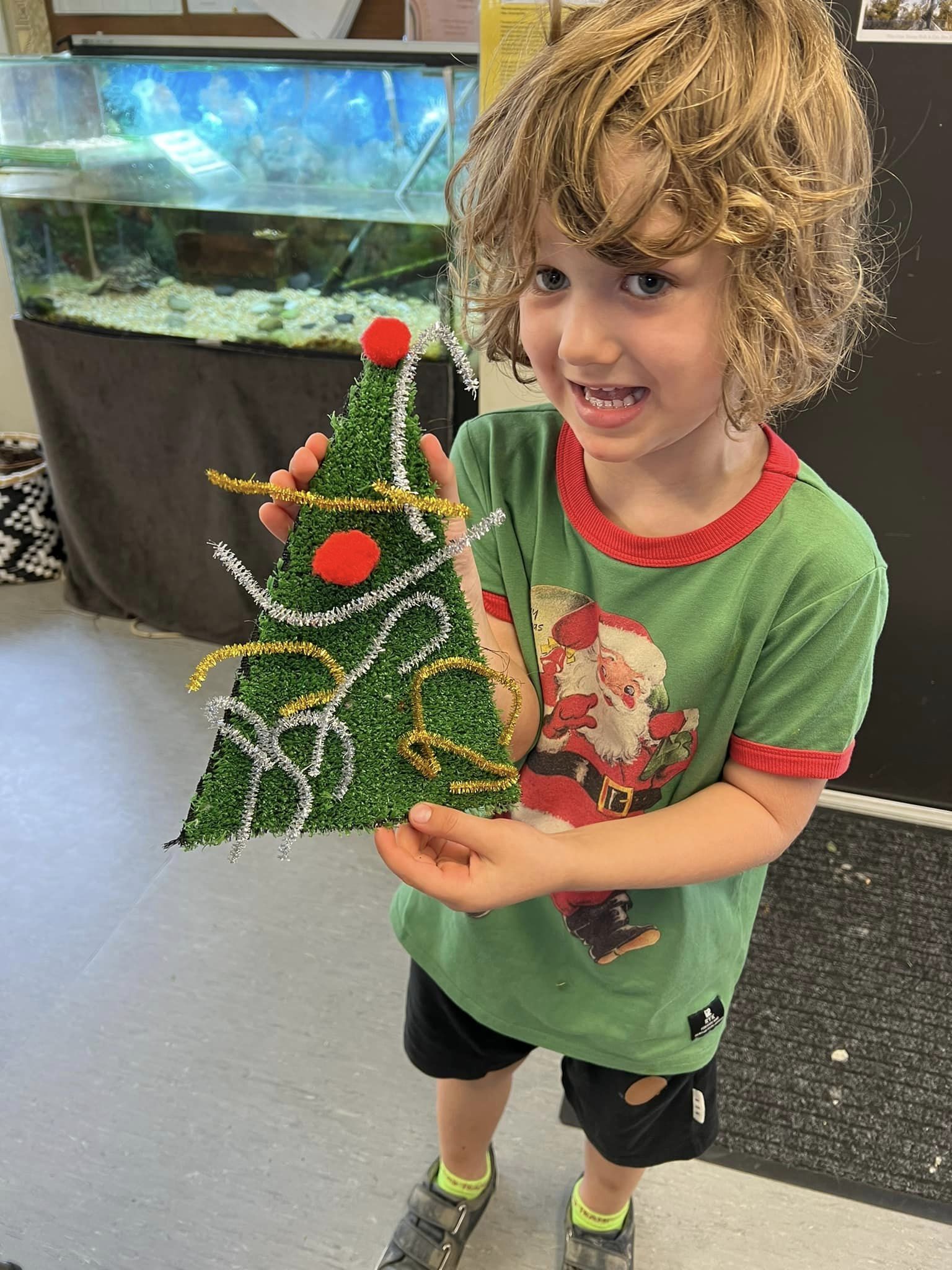 A young boy is holding a christmas tree made out of pipe cleaners.