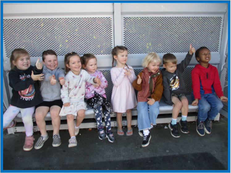 A group of children are sitting on a bench and giving a thumbs up