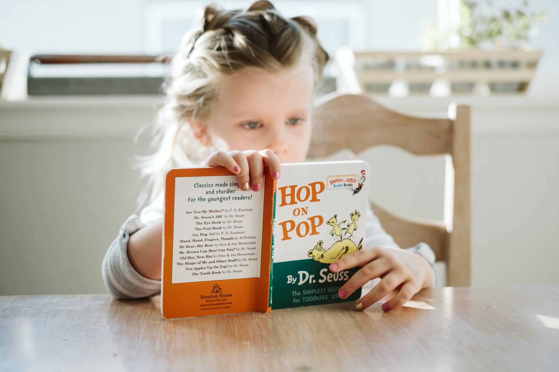 A little girl is reading a book called hop on pop.