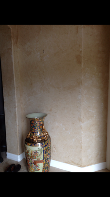 A tall decorative vase on a corner wall with off-white trim. Walls have a mottled tan finish.