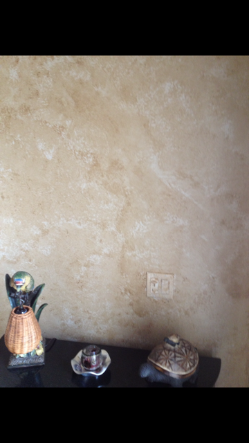 Beige textured wall with black table and three decorative objects.