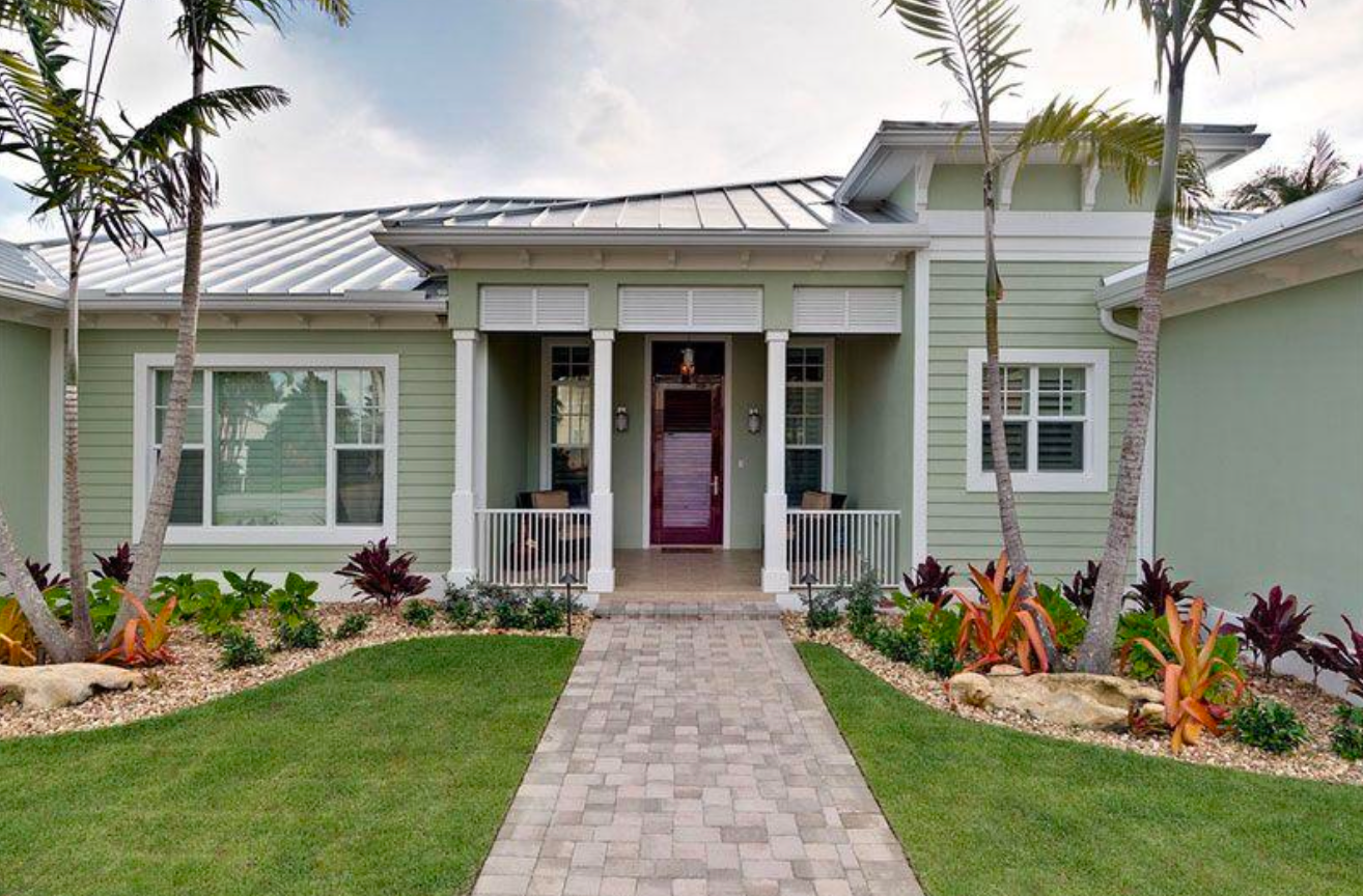 Green house with a red door, brick walkway, and palm trees.