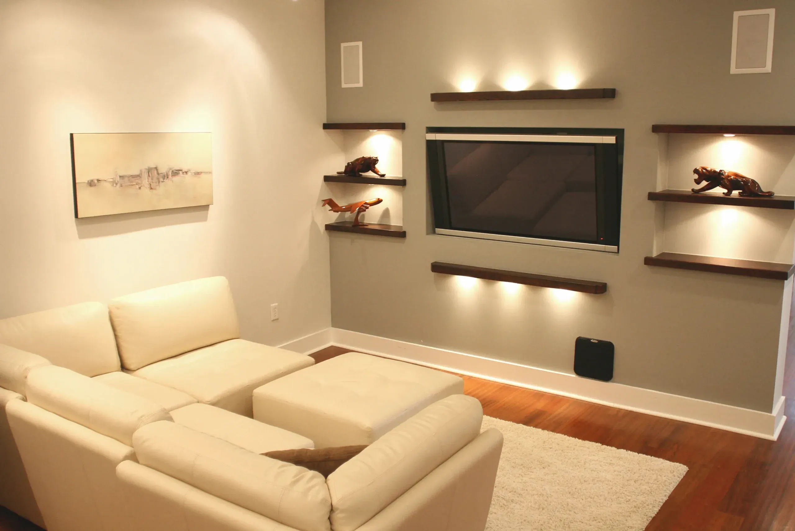 A modern living room with a sectional sofa, built-in TV, shelves, and warm lighting.