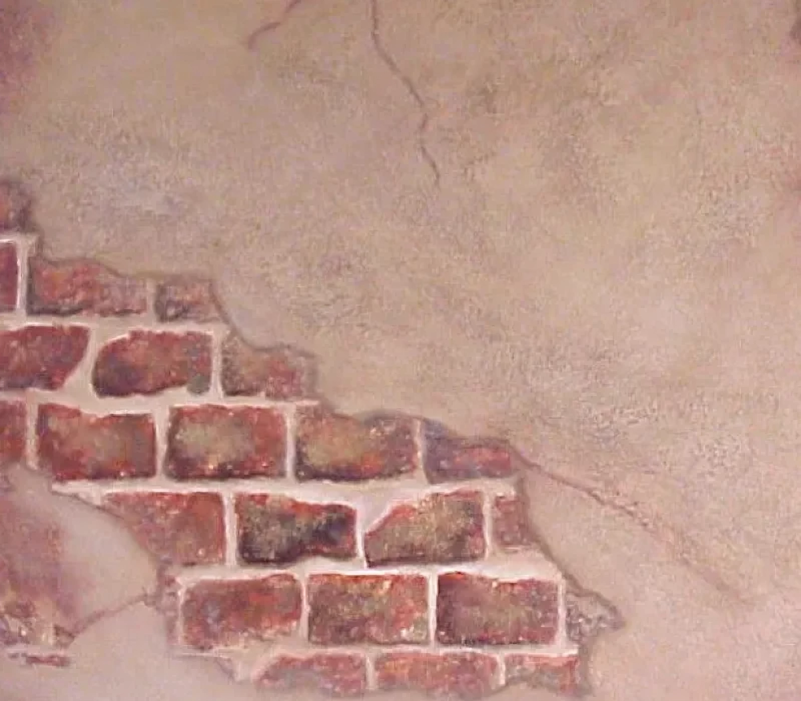 Brick wall partially covered by peeling plaster. Red-brown bricks with white mortar; beige plaster with cracks.
