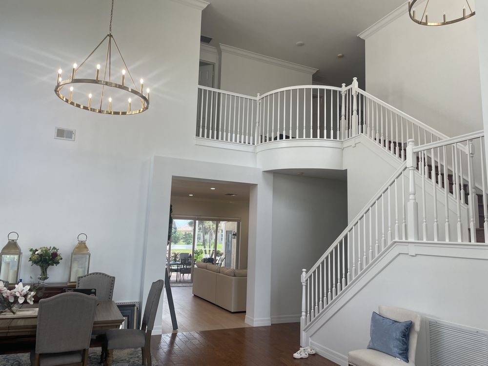A spacious, white-walled foyer with a staircase, balcony, and chandelier.