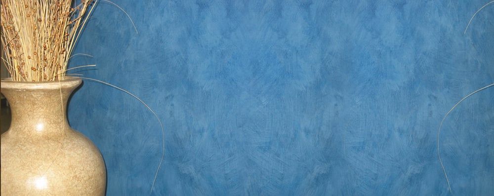 A tan vase with dried grasses against a blue textured background.