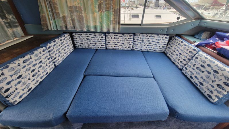 A boat's helm seat. Beige and gray cushioned seat. Blue water and trees in the background.