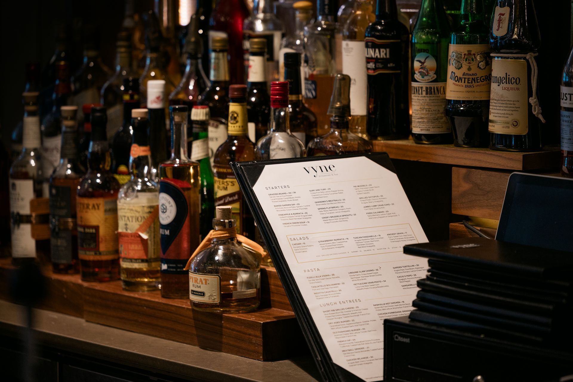 Bar shelf with liquor bottles and a cocktail menu beside a piano keyboard
