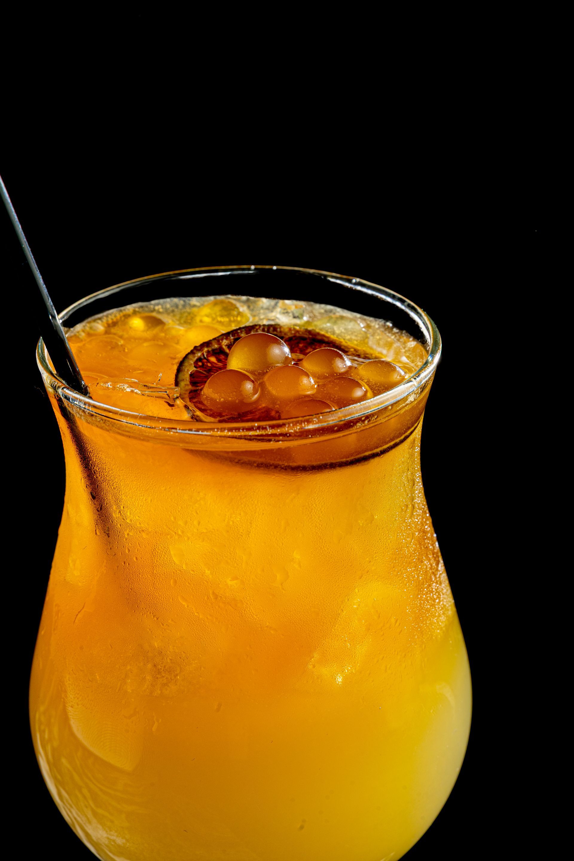Orange cocktail with ice and a straw in a clear glass against a black background at Vyne