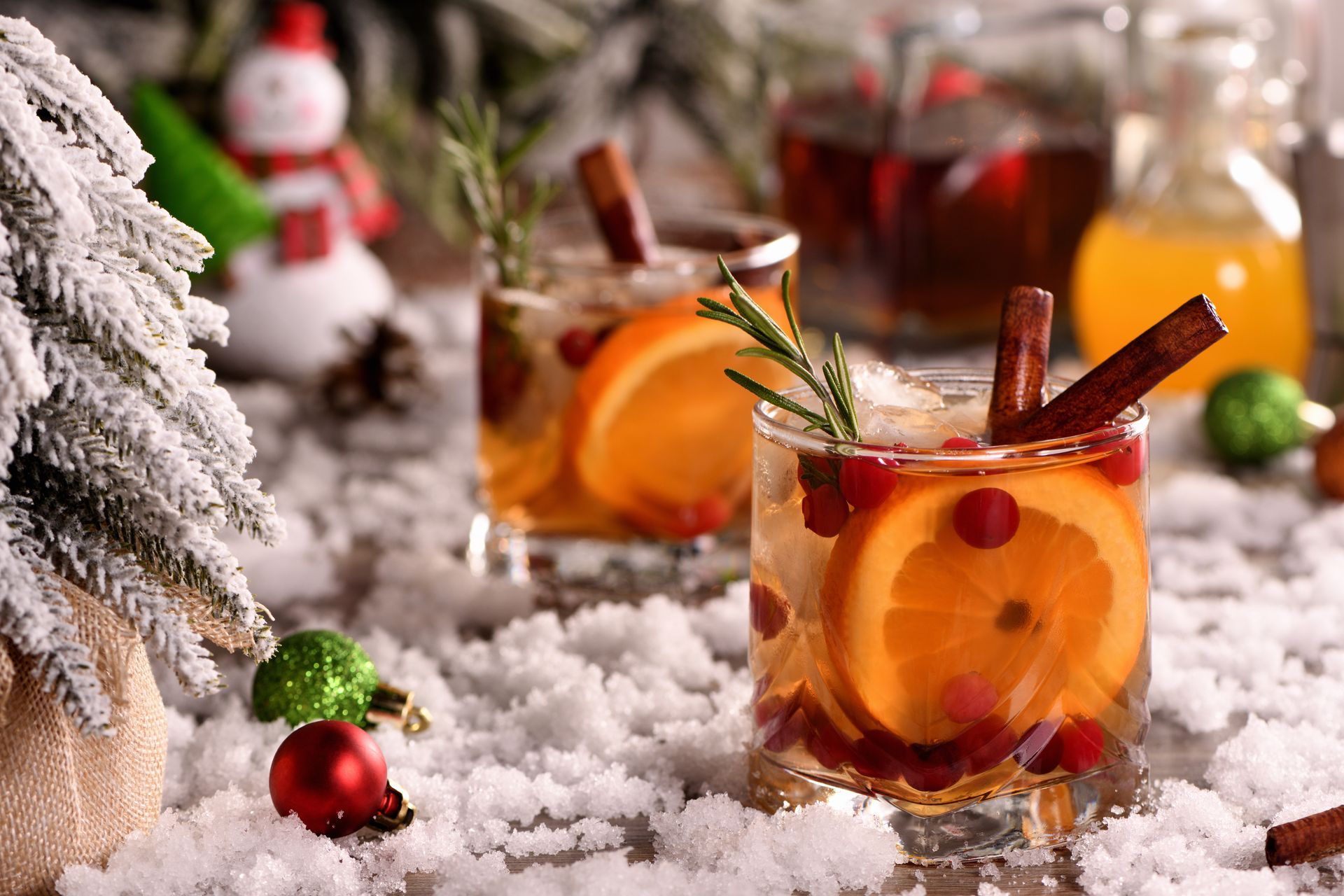 Christmas drinks with orange slices, cinnamon sticks, and rosemary on a snowy table