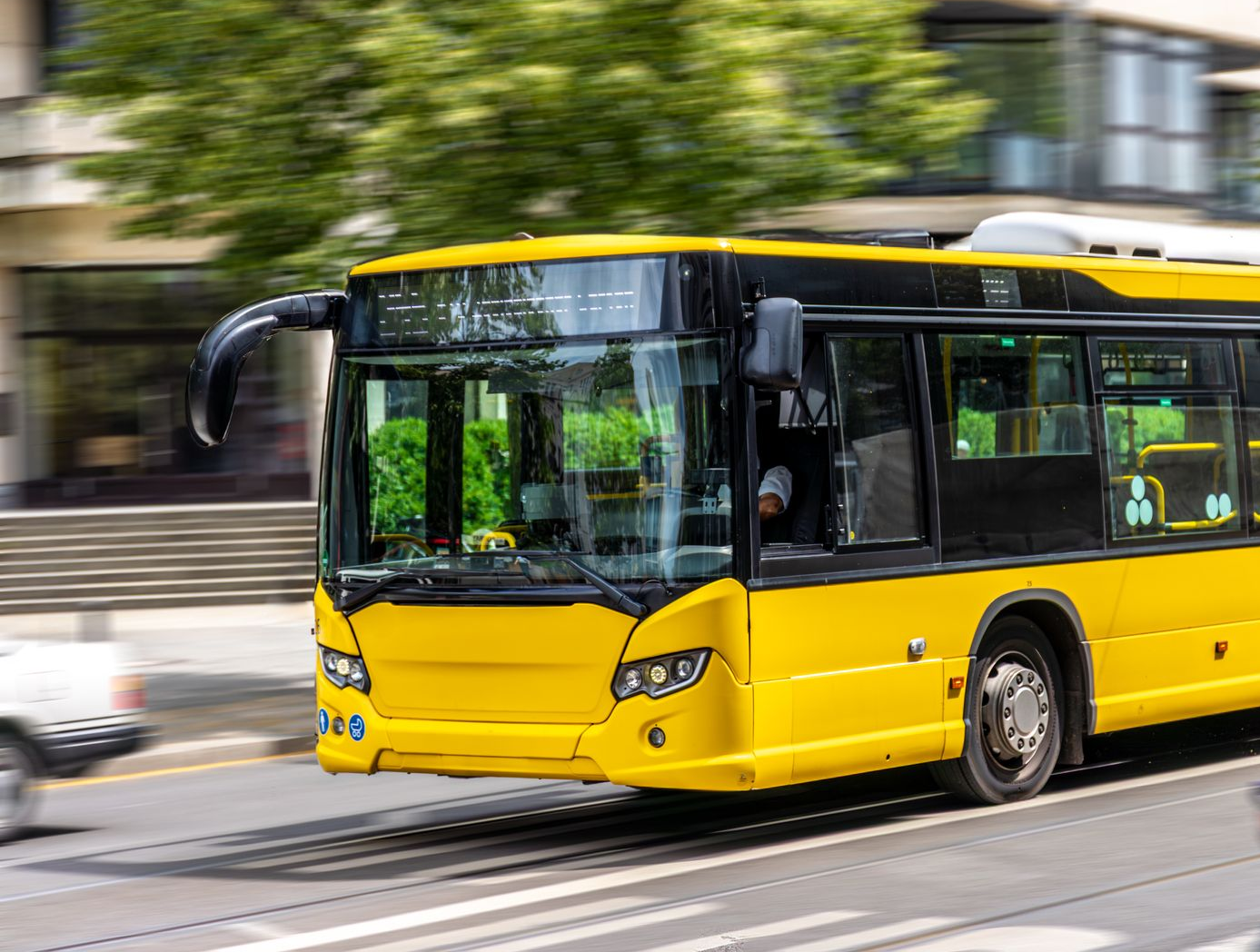 Gul stadsbuss som kör på en väg med träd i bakgrunden. Körkortsintyg av läkare krävs för att köra buss.