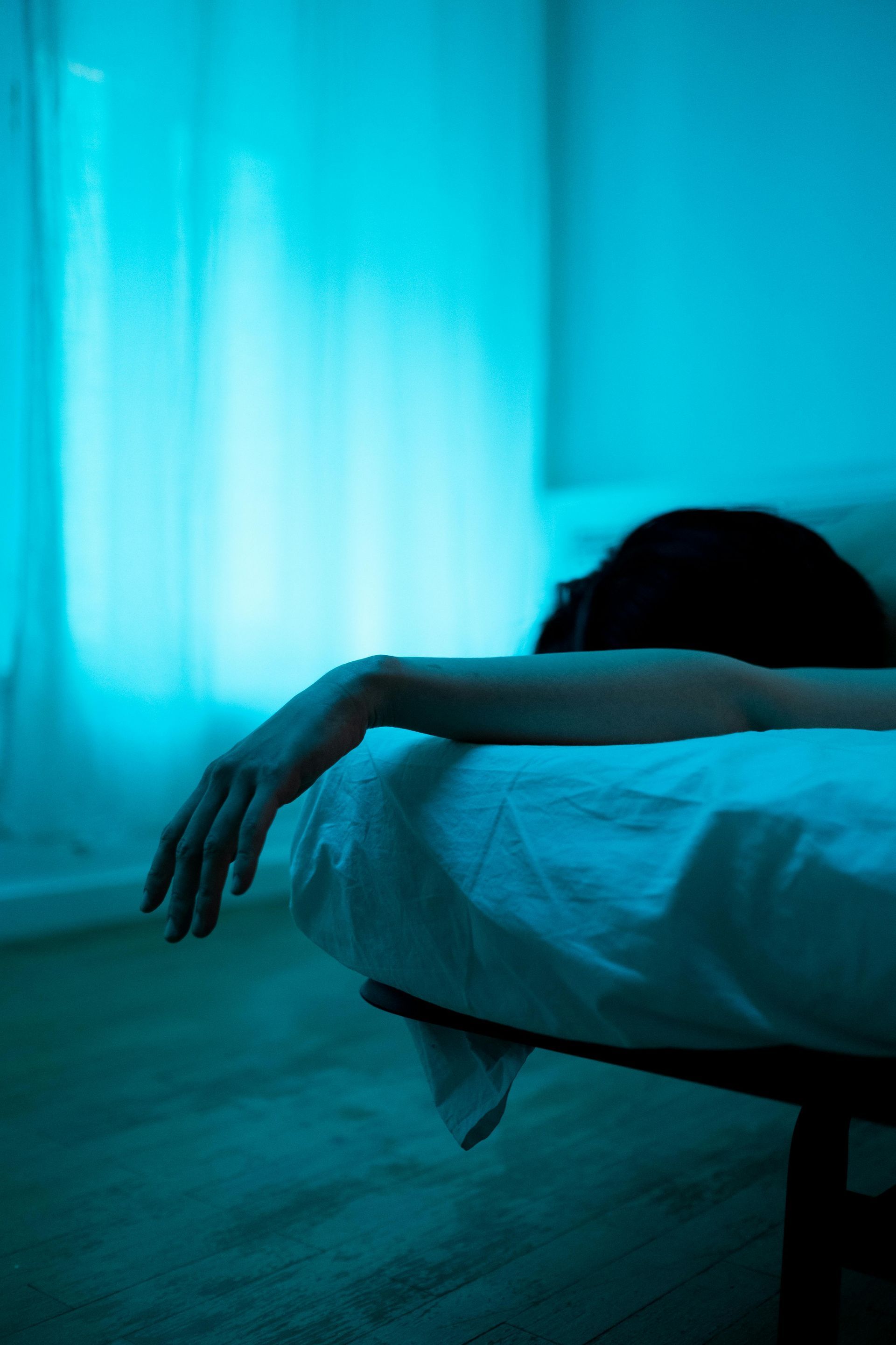 En persons arm draperad över en säng. Rummet har en blå nyans.