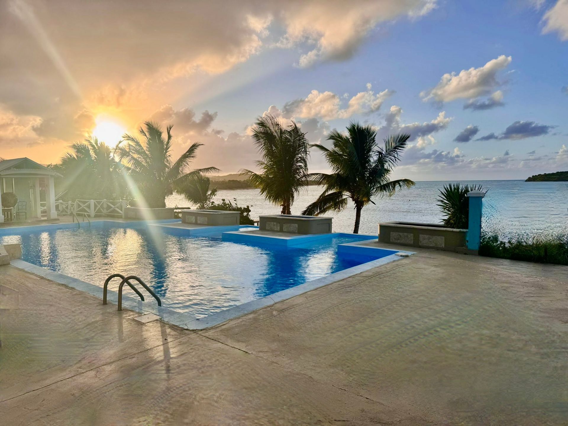 A large swimming pool with a view of the ocean at sunset.