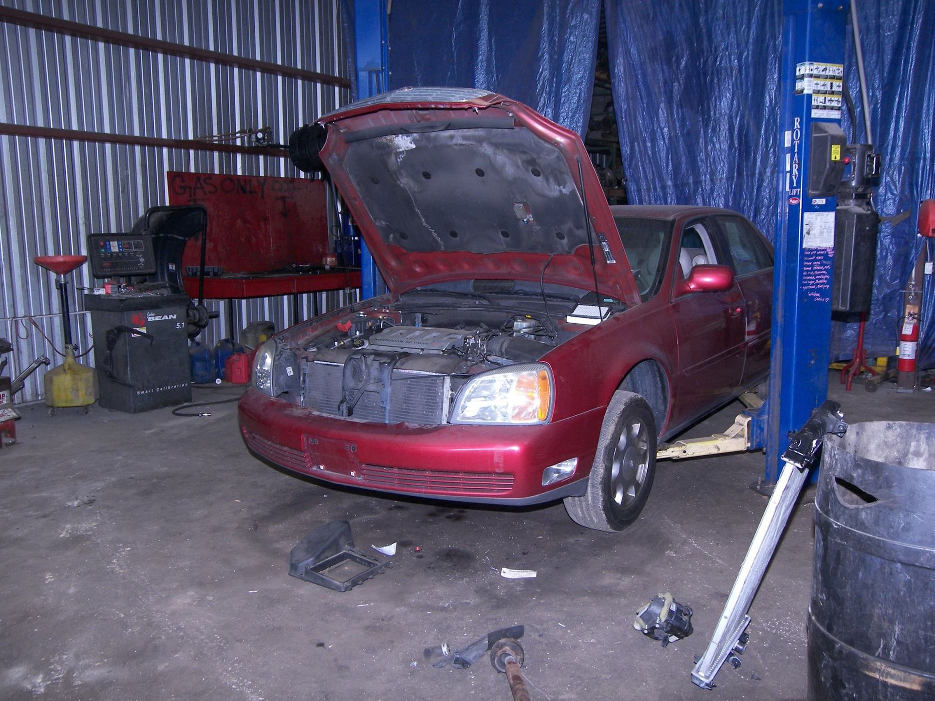 A red car with the hood up is on a lift in a garage