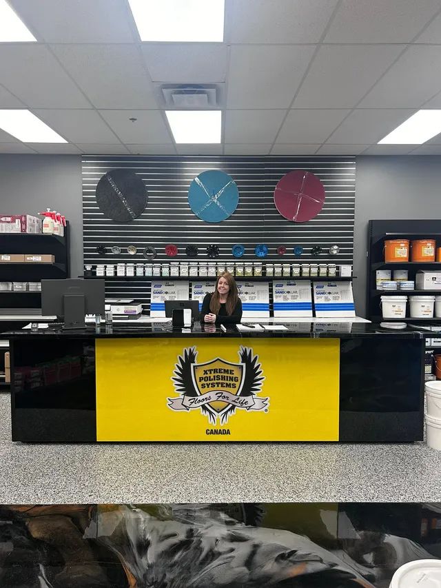 Store counter with a person behind it, black and yellow front panel, and shelves of products in the background.