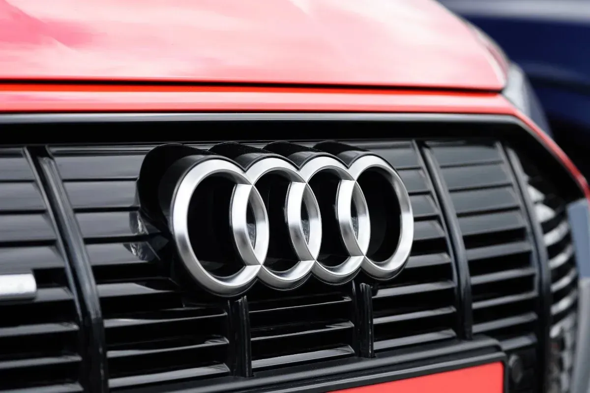 Close-up of the Audi logo on a black grille with a red car hood above