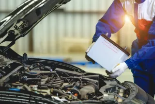 Mechanic in blue overalls checking engine oil under open car hood in a garage