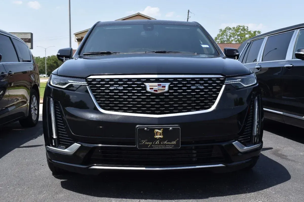Black Cadillac SUV parked outdoors, front view with chrome grille between two vehicles.