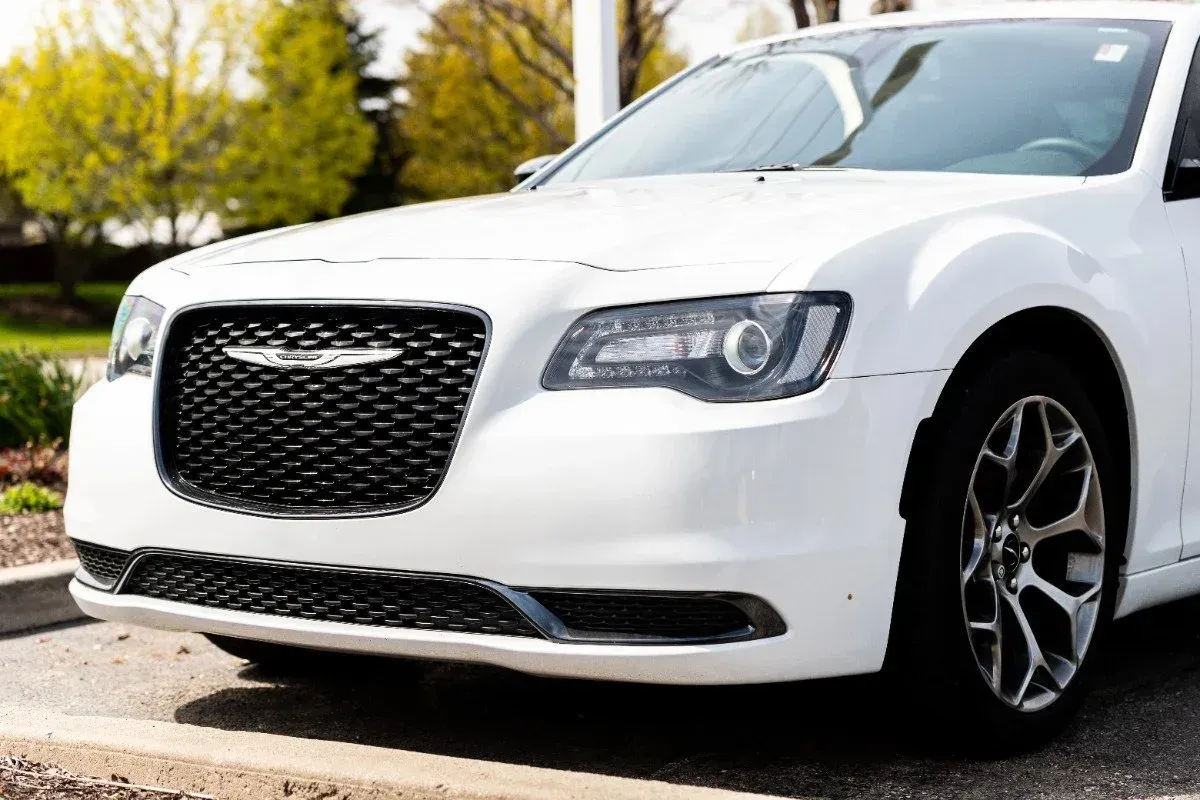 White Chrysler sedan parked on a street with trees in the background
