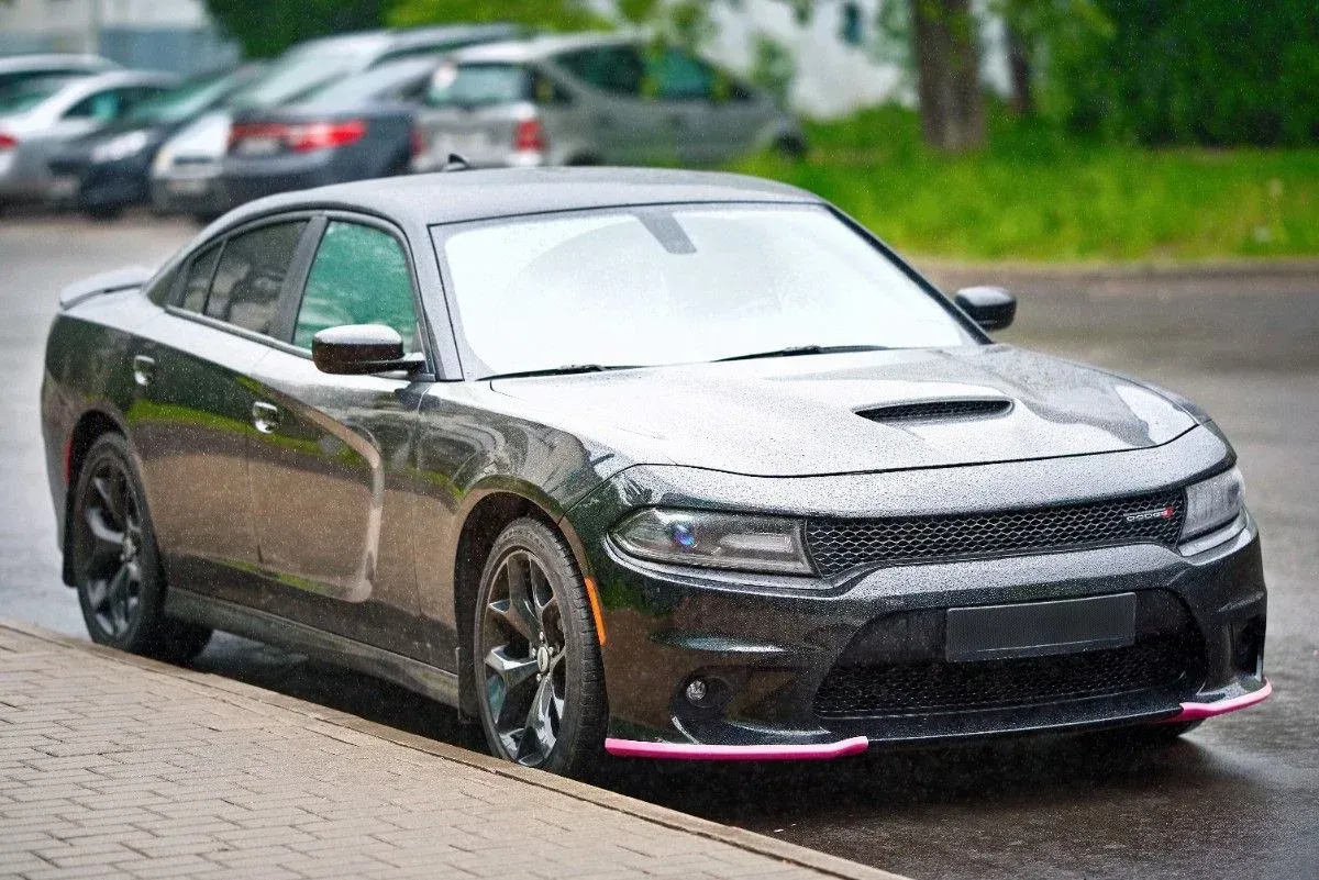 Black sports sedan parked on a wet street, front three-quarter view, with a pink front splitter.