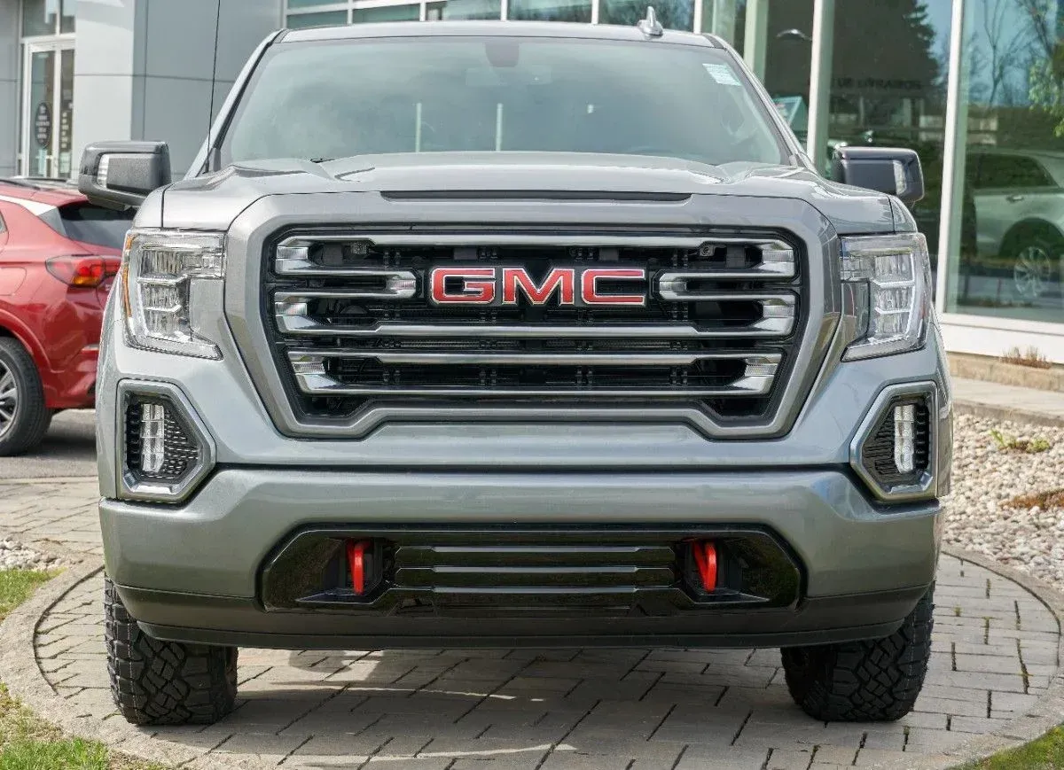Front view of a silver GMC pickup truck parked outdoors, with red tow hooks and a chrome grille.