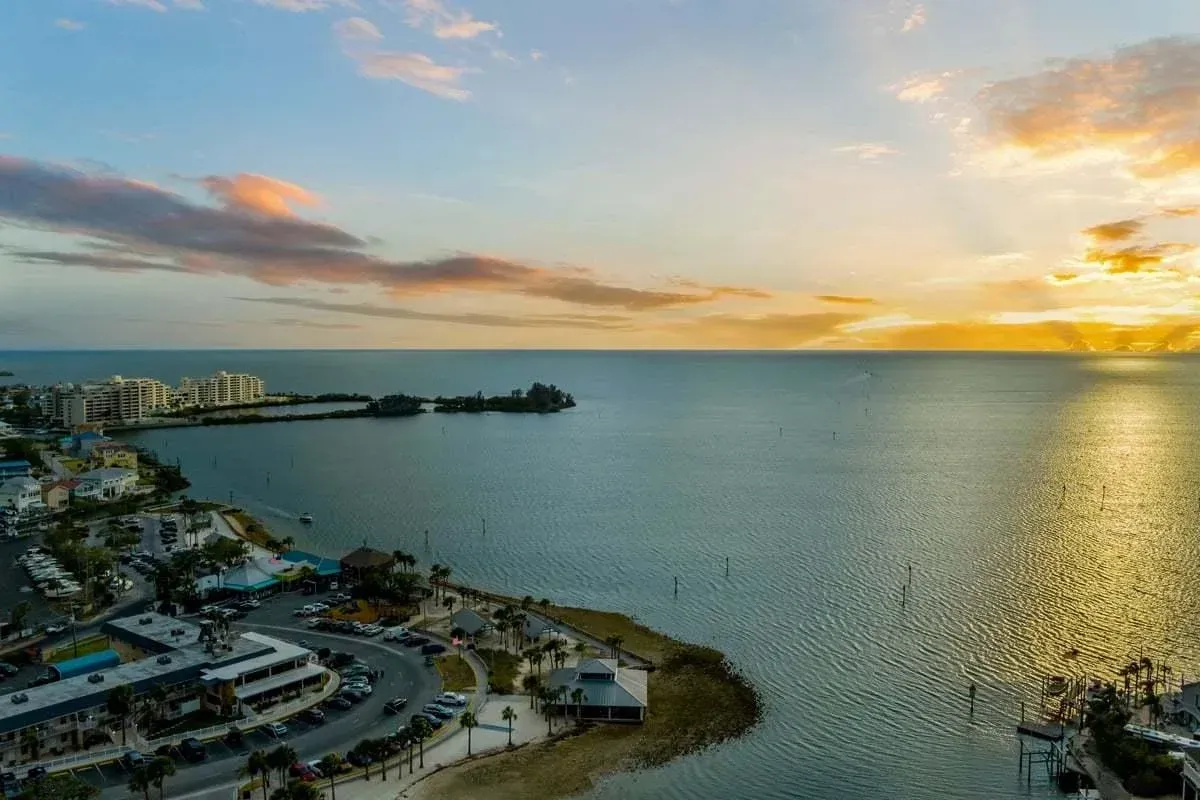 Sunset over a calm bay with coastal buildings and a golden reflection on the water
